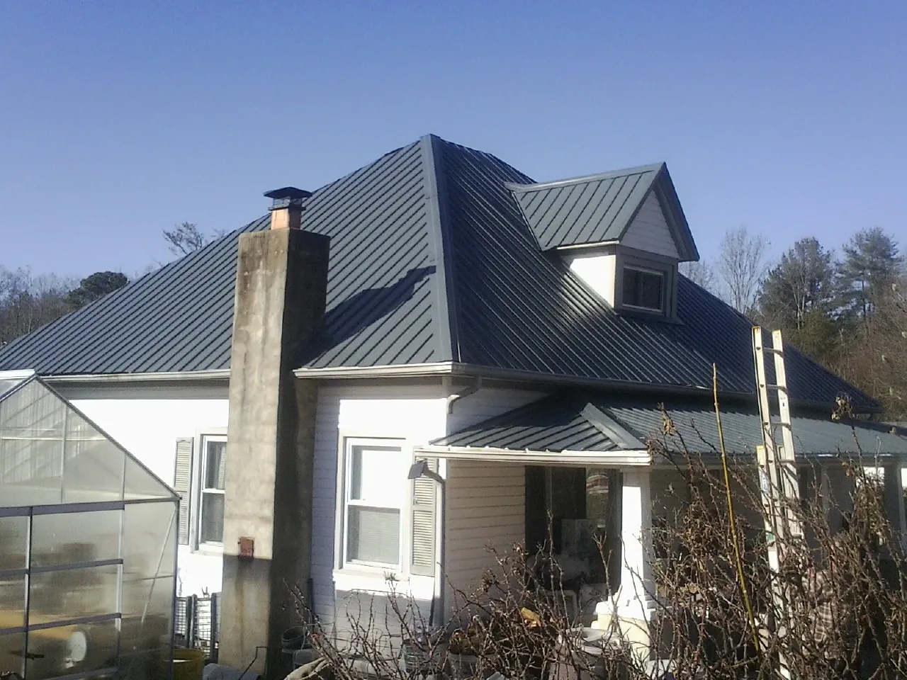 Dark blue standing seam metal roof on a white farmhouse with dormer — Slate & Tile Roof Repair by Roofing Brothers in Gowen
