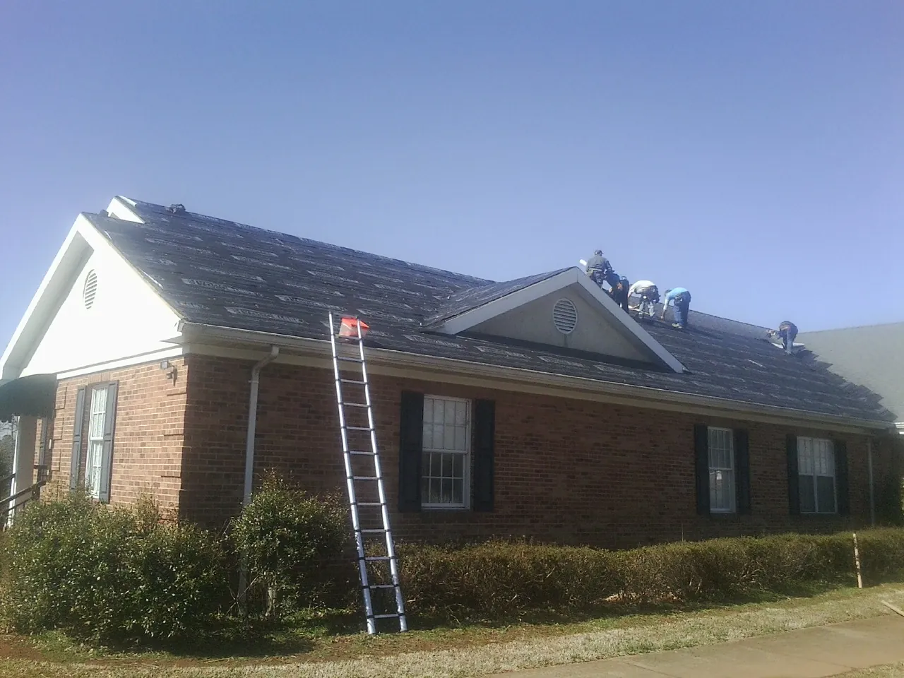 Crew tearing shingles off a brick ranch roof with a ladder set — Emergency Roof Repair work by our crew in Gowen