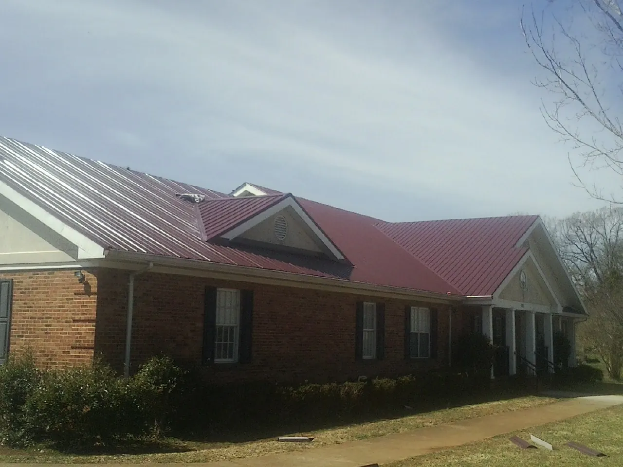 Red metal roof with gabled entries on a long brick building, from a Hail Damage Roof Repair job in Gowen