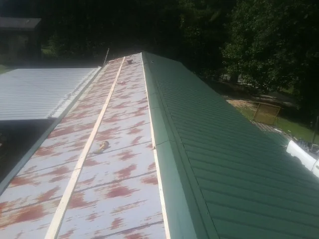Old rusted panels beside newly installed green metal roofing — Wind Damage Roof Repair by Roofing Brothers in Gowen