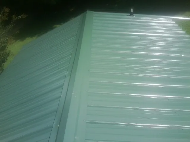 New green metal panels meeting at the ridge of a roof — Flat Roof Repair work by our crew in Gowen