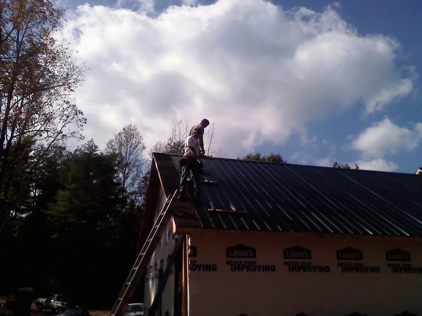 Roofer fastening dark metal panels high against a cloudy sky, from a Roof Inspection job in Gowen