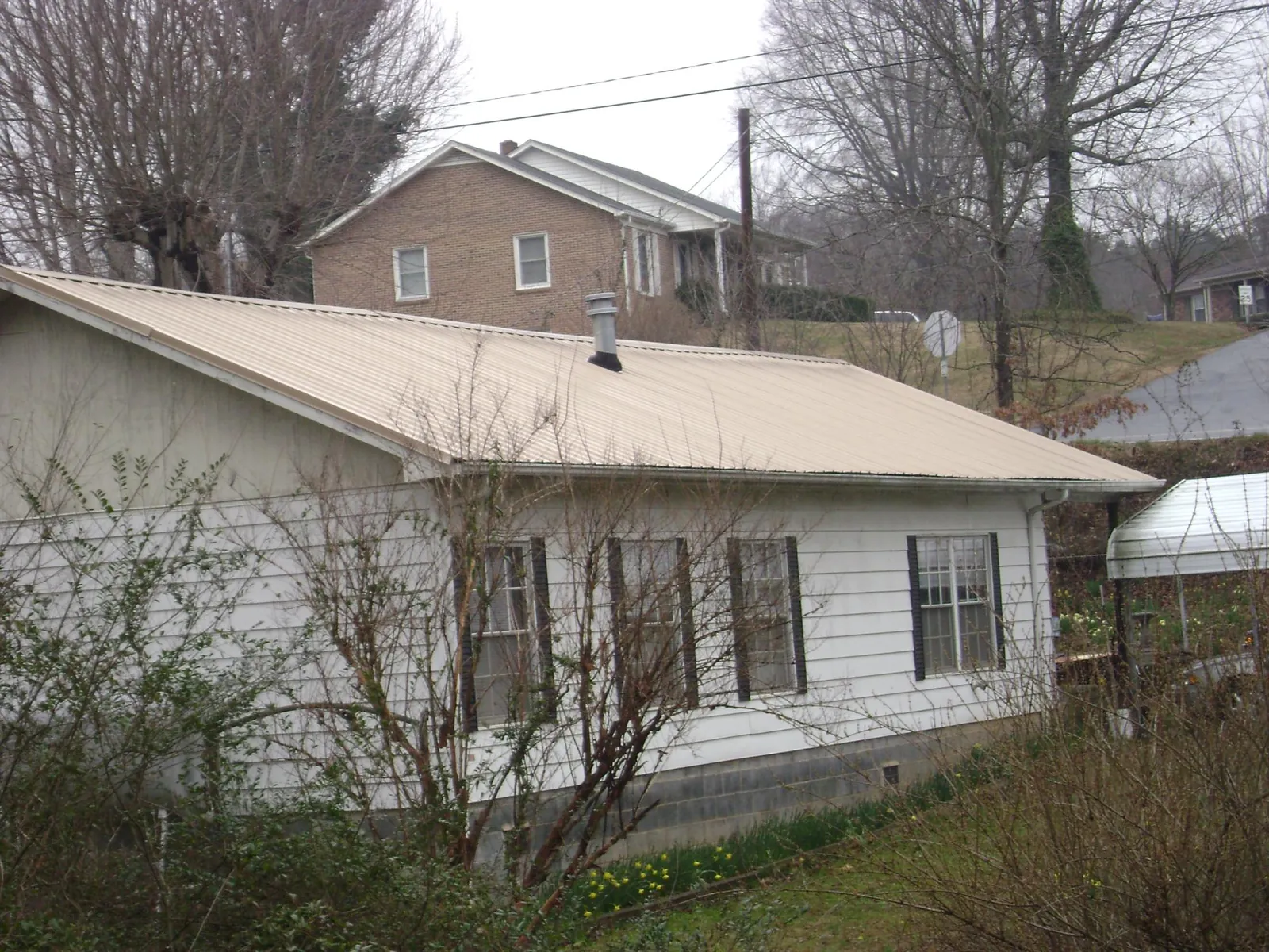 Tan metal roof on a white sided house set into a hillside — Commercial Roofing by Roofing Brothers in Gowen