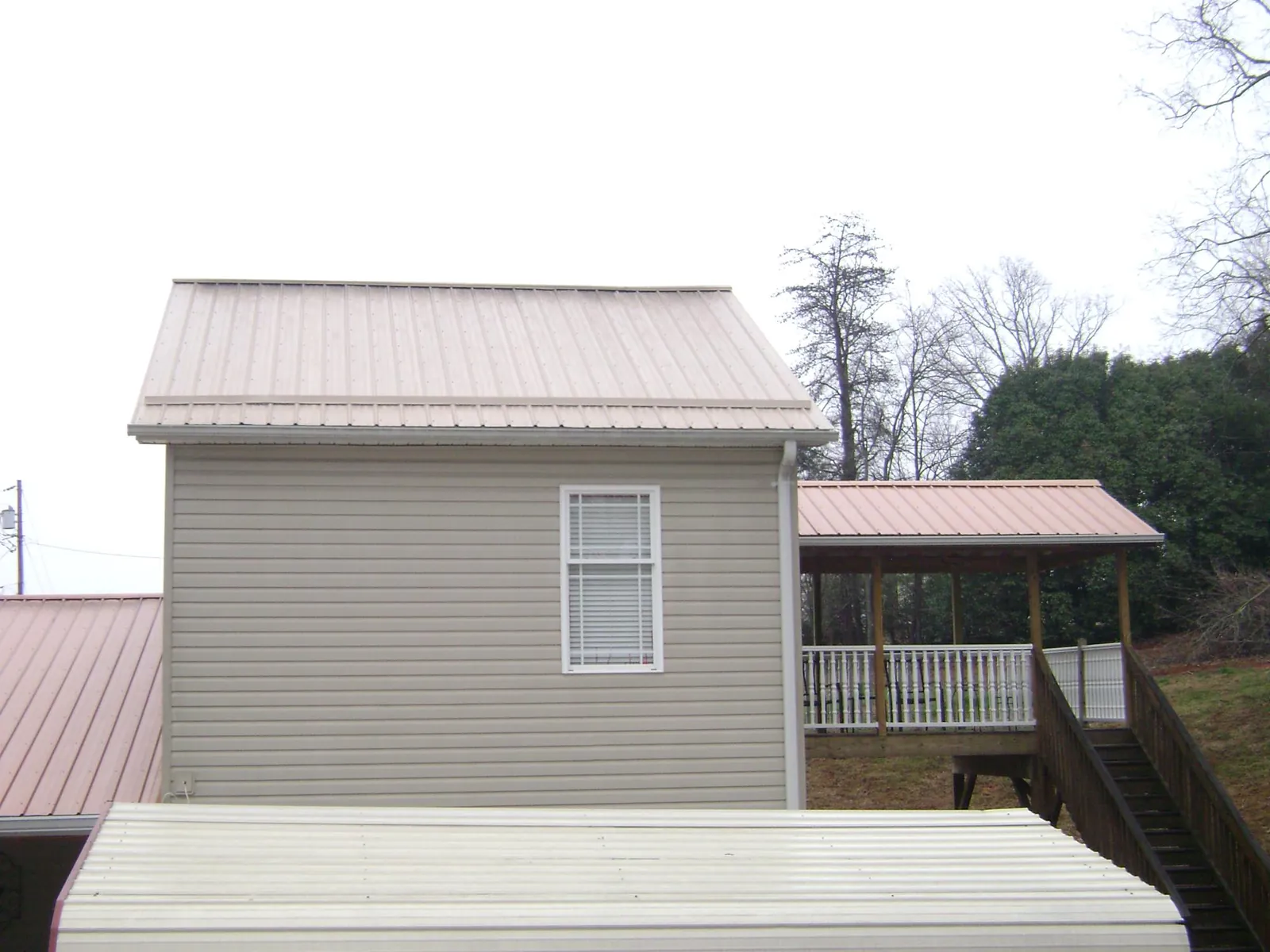 Tan metal roofs on a two story addition and attached porch, from a Roof Replacement job in Gowen